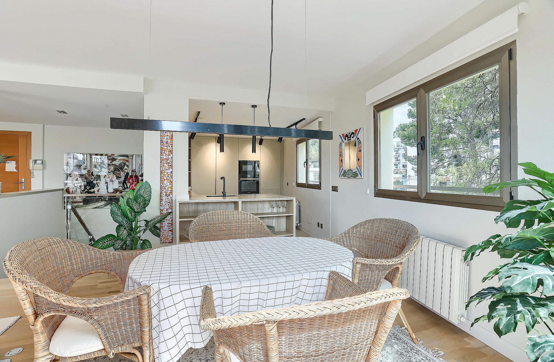 Dining room interior featuring a round table with patterned tablecloth surrounded by four rattan armchairs, lit by a linear pendant light.