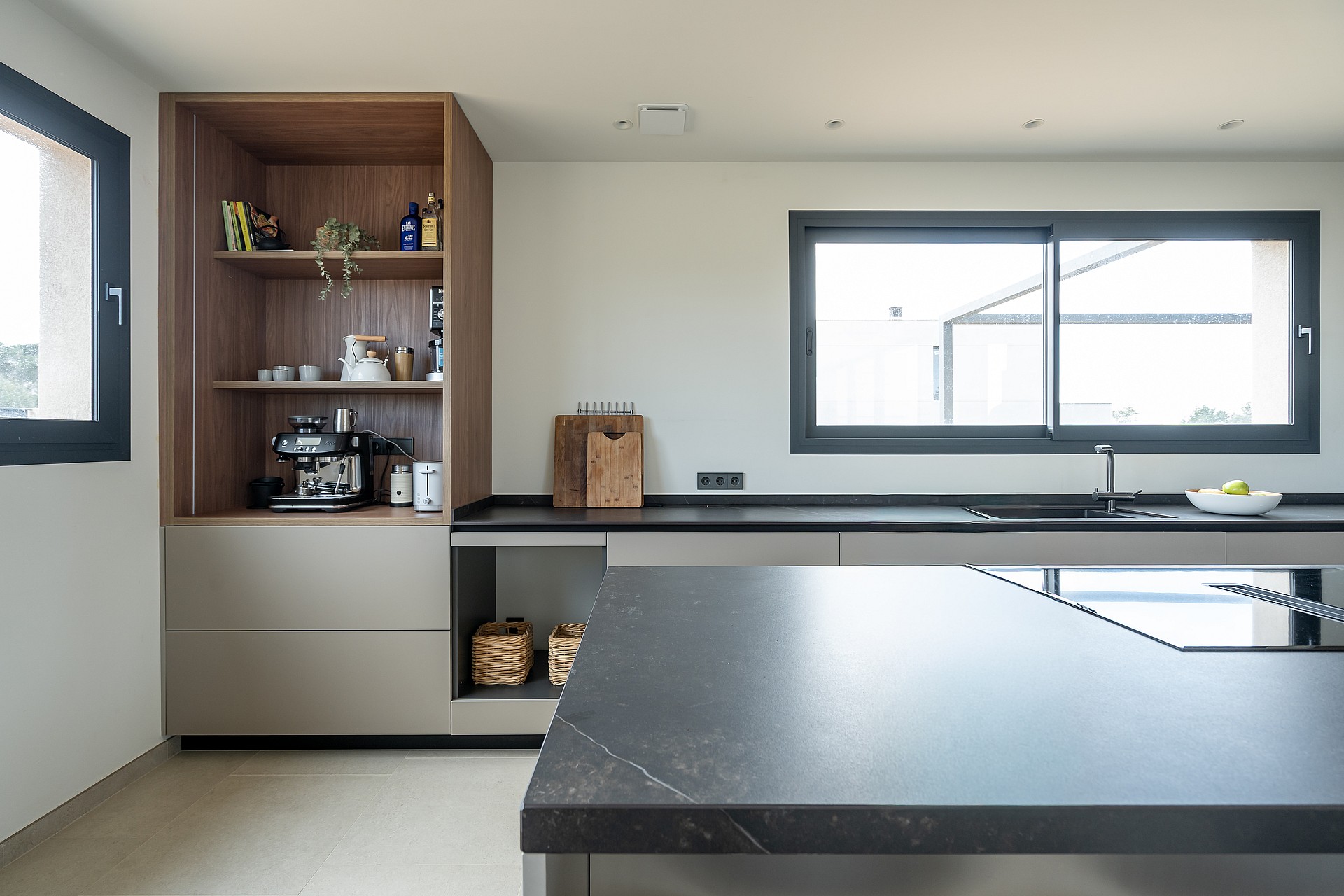 Contemporary kitchen featuring matte grey cabinets, dark stone countertops, wooden shelving unit, and integrated appliances.
