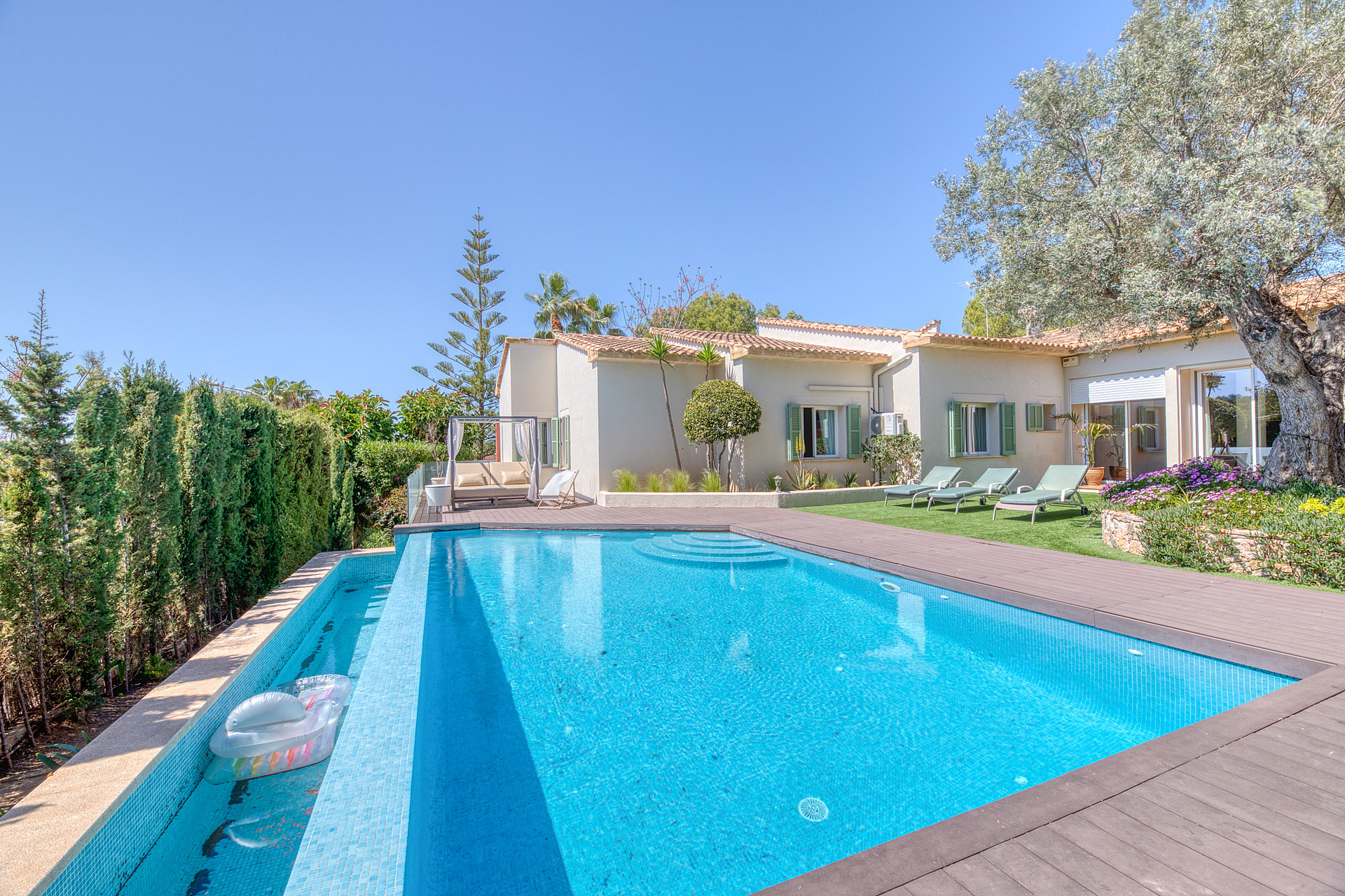 Exterior view of a Mediterranean villa with a rectangular swimming pool, wooden decking, and landscaped gardens in Santa Ponsa.