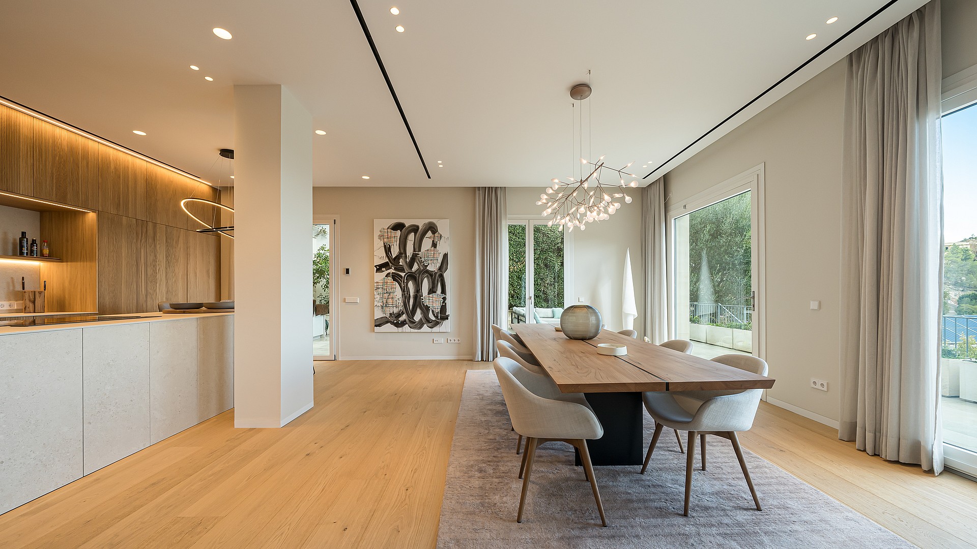 Dining room with a long wood table, modern sculptural chandelier, light oak flooring, and neutral walls in an open-plan villa.