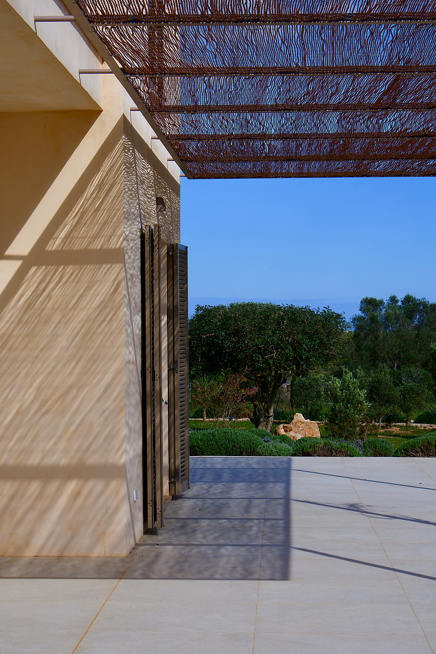 A modern outdoor terrace in Santanyí featuring a geometric laser-cut metal pergola casting intricate shadows on stone walls.