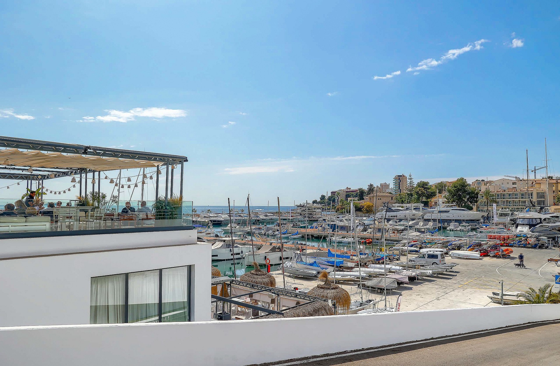 An elevated view overlooking a busy marina and harbor with small boats, viewed from a white modern building terrace.