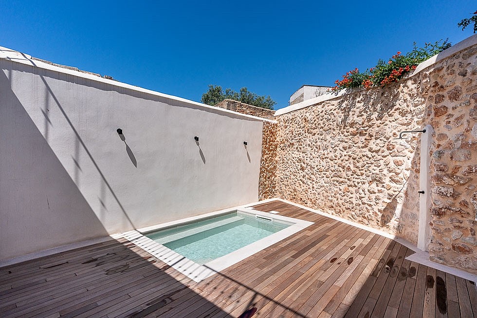 A small rectangular plunge pool set into a wooden deck inside a private courtyard with high white and stone walls.