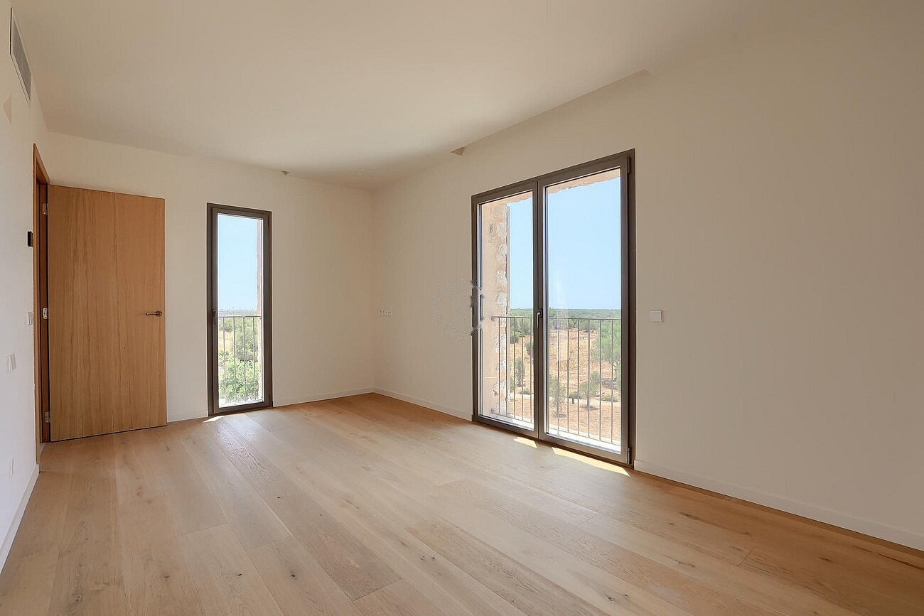 Unfurnished bedroom with light oak flooring, white walls, and glass doors opening to a balcony with mountain landscape.