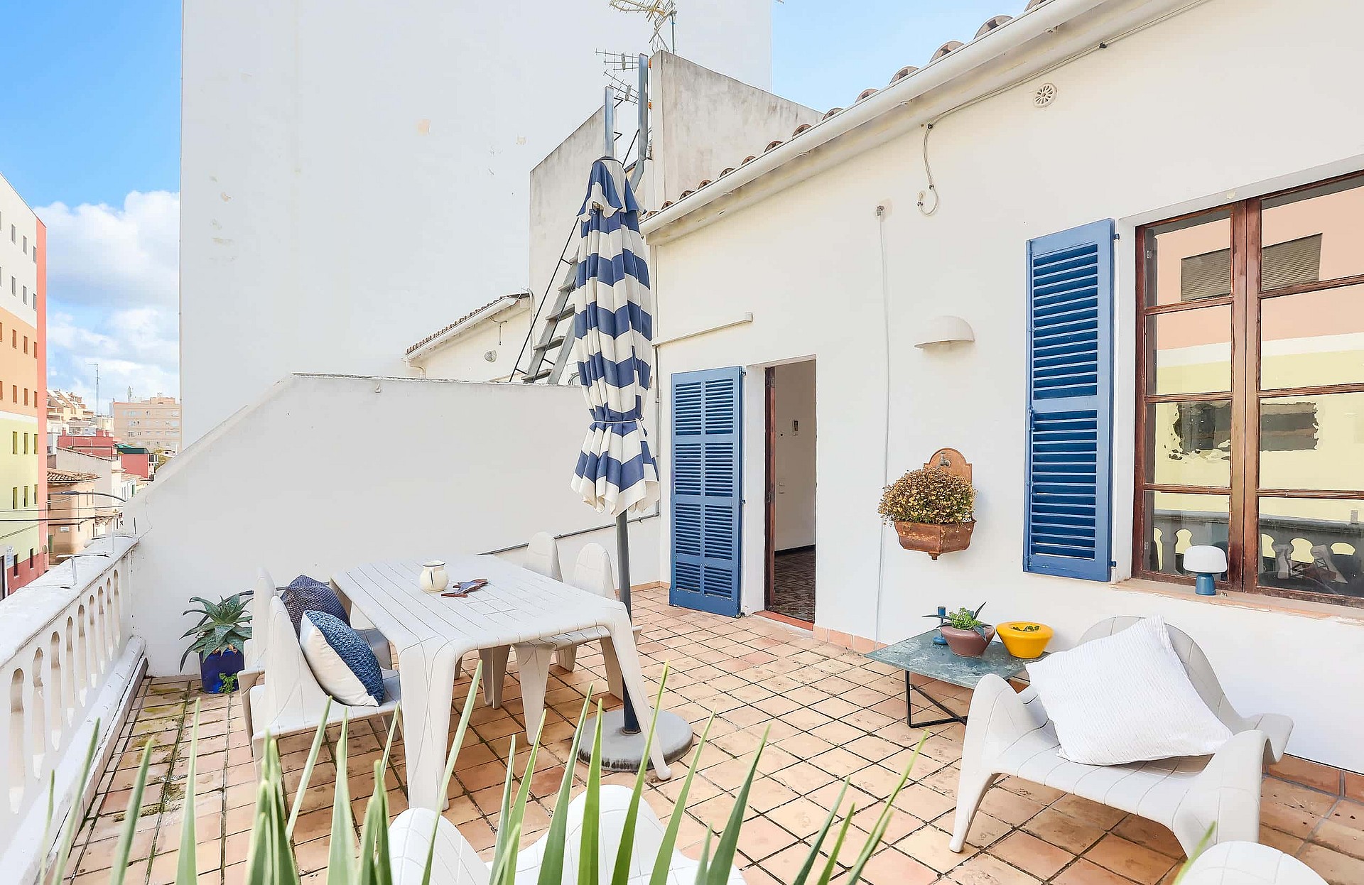 Outdoor terrace of a penthouse in Santa Catalina with white tiled flooring, blue shutter windows, and dining furniture.