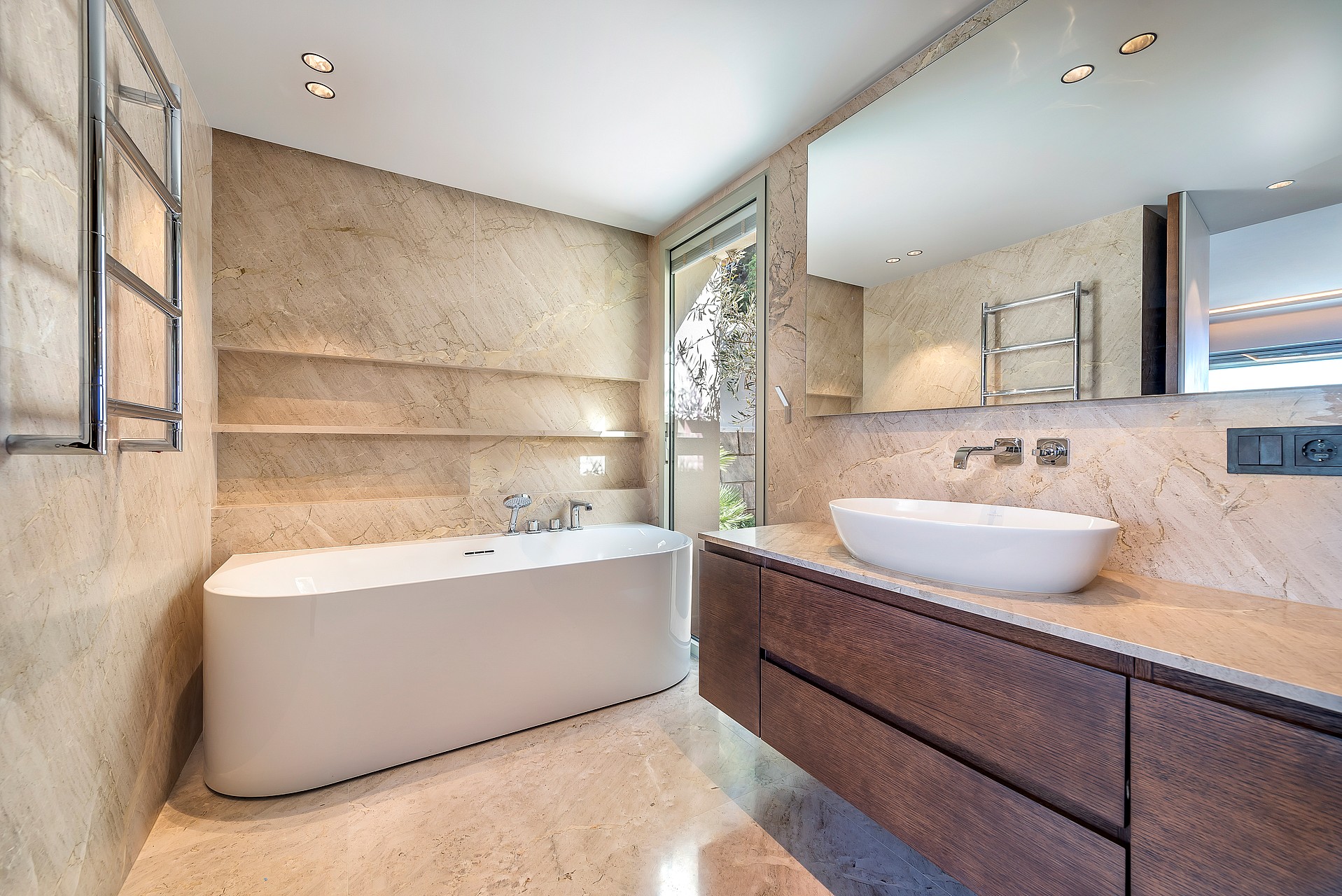 Contemporary bathroom featuring a dark wood vanity, white vessel sink, and large wall-to-wall mirror with travertine tile walls.