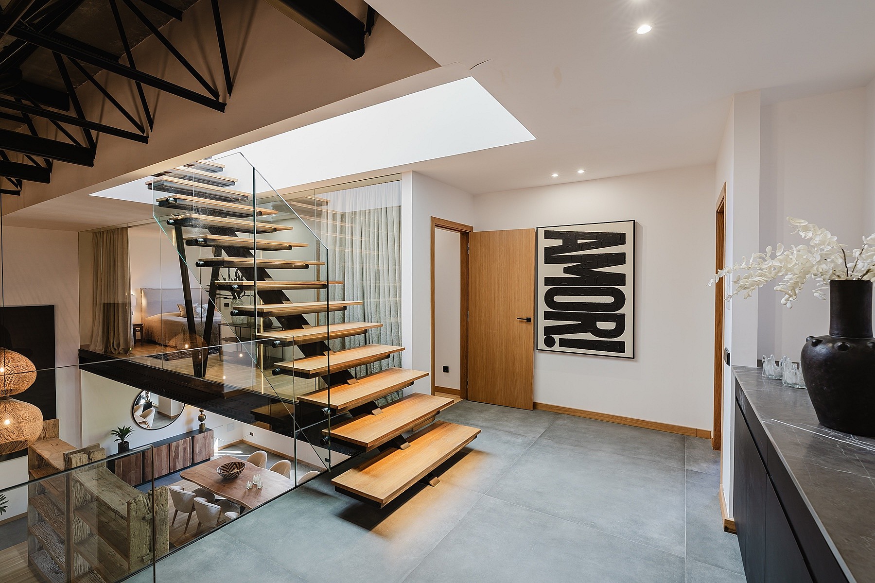 A modern floating staircase with wood treads and a glass railing connects levels in an apartment, viewed from a landing.