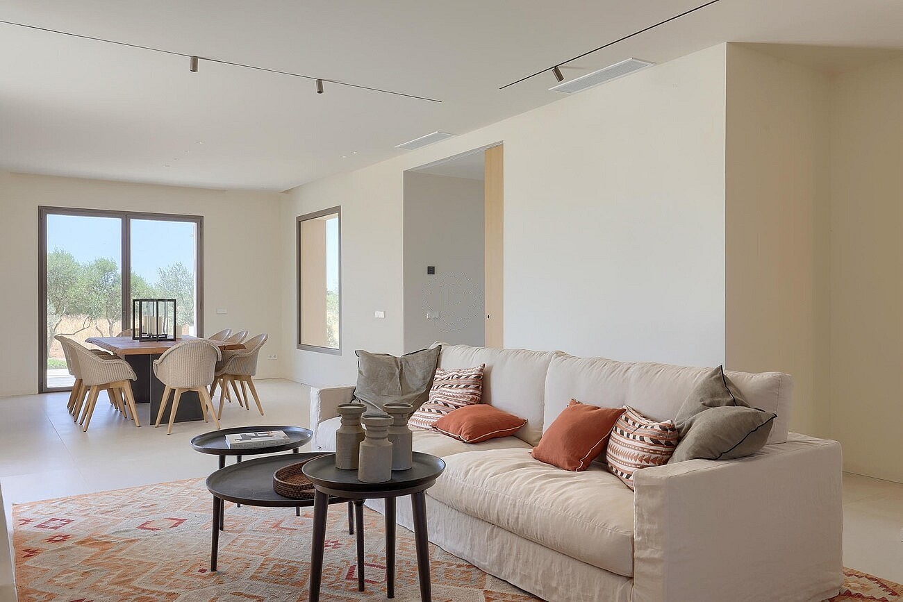 An open-concept living and dining space with a cream fabric sofa, nested coffee tables, and a wooden dining set near a large window.