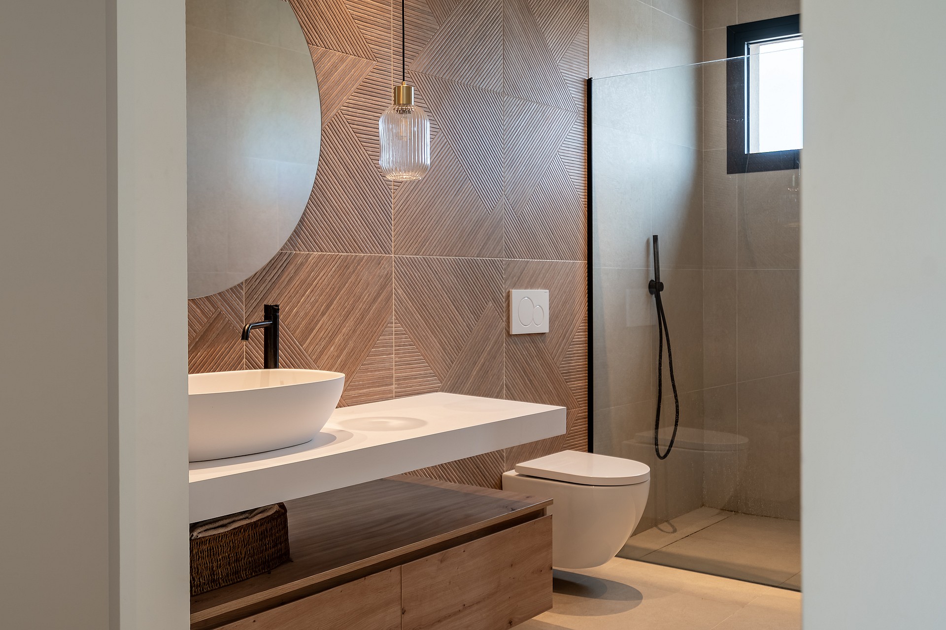 Modern bathroom interior with white vessel sink on a floating vanity, a circular wall mirror, and a geometric-textured accent wall.