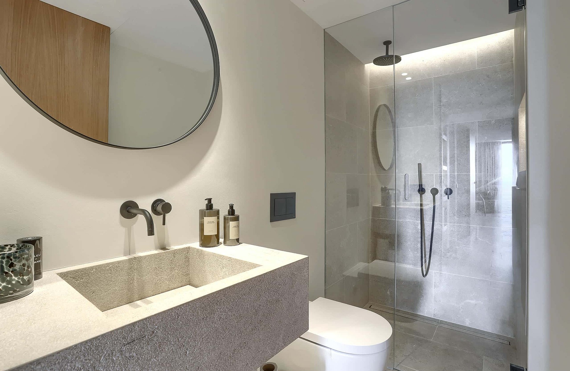 Contemporary bathroom featuring a grey stone vanity with a vessel sink, a circular mirror, and a walk-in glass shower.