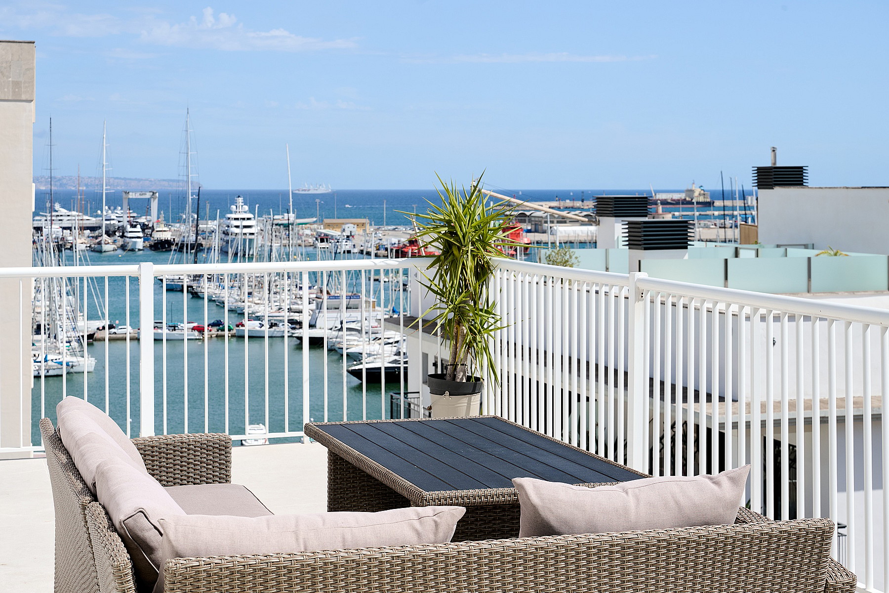 A rooftop terrace with wicker furniture overlooking a marina filled with boats under a clear blue sky in Santa Catalina.