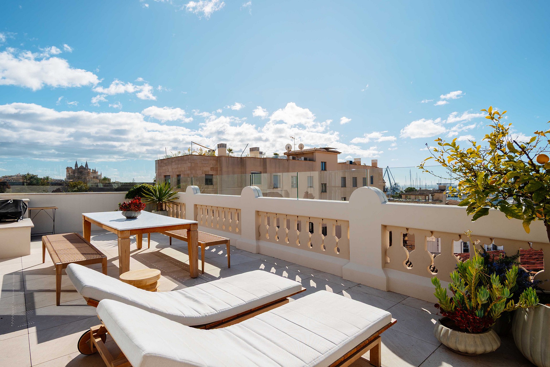 A sunny rooftop terrace in Santa Catalina with white sun loungers, a wooden dining table, and a decorative stone balustrade.