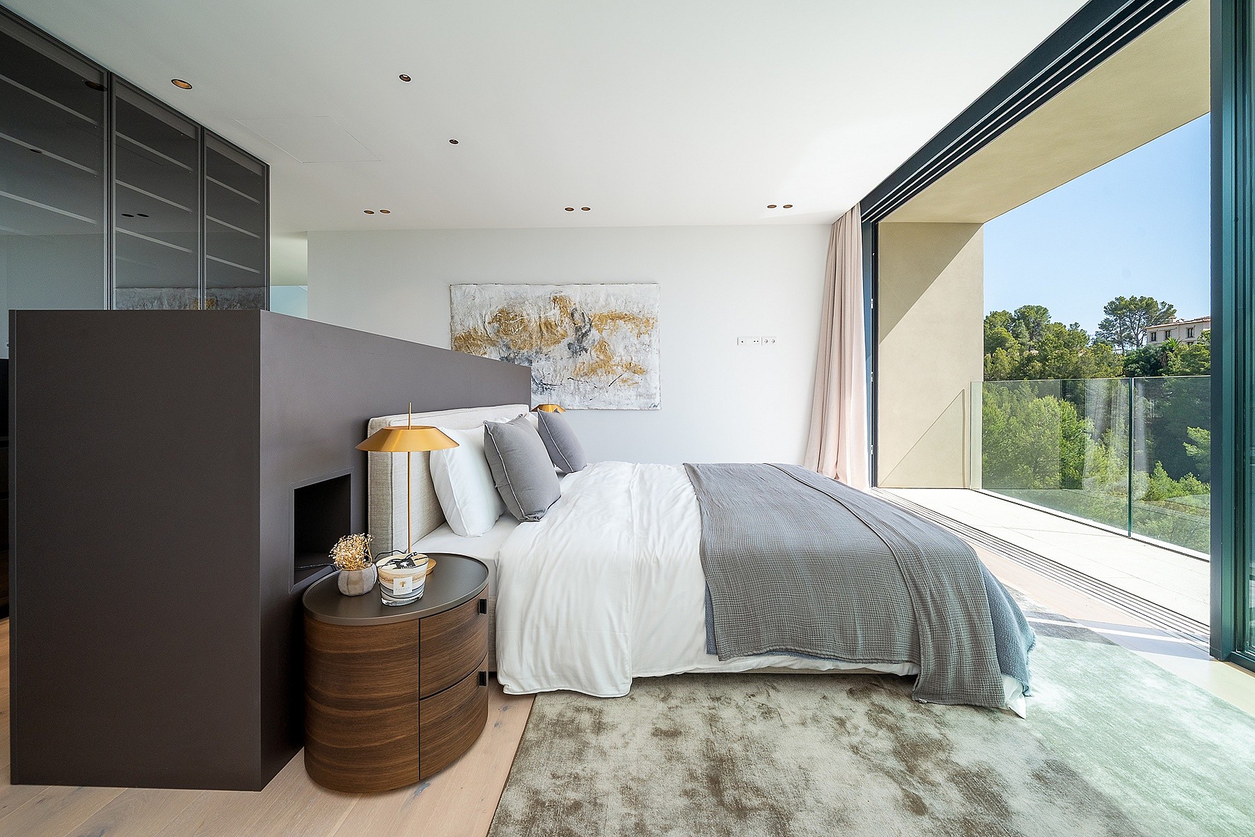 A modern bedroom featuring a bed placed against a dark partition, with floor-to-ceiling glass doors opening to a terrace.