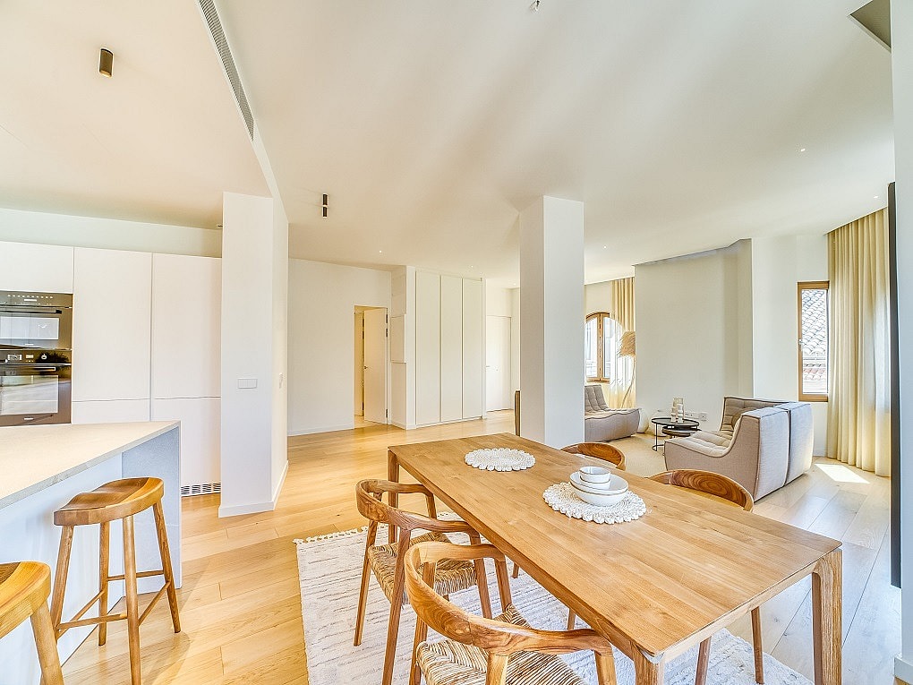 Open-plan room featuring a light wood dining table with curved wooden chairs and a minimalist kitchen island with bar stools.