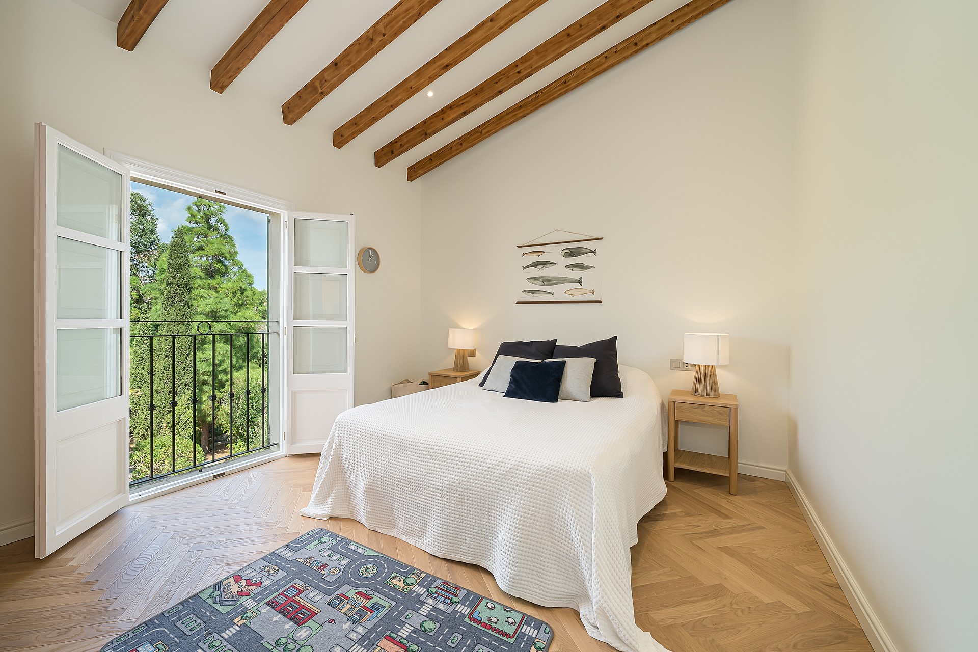 Bright bedroom featuring slanted timber ceiling beams, herringbone oak floors, and glass doors opening to a garden view.