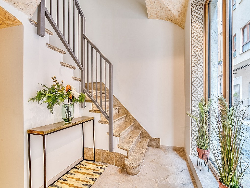 Interior entrance hall featuring a light stone staircase with a dark metal railing, a slim console table, and patterned tiles.