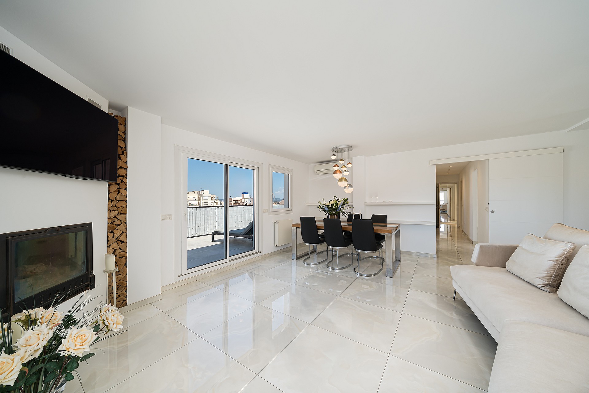 Bright open-plan living room with white marble floors, a recessed fireplace, and a dining set leading to a terrace.