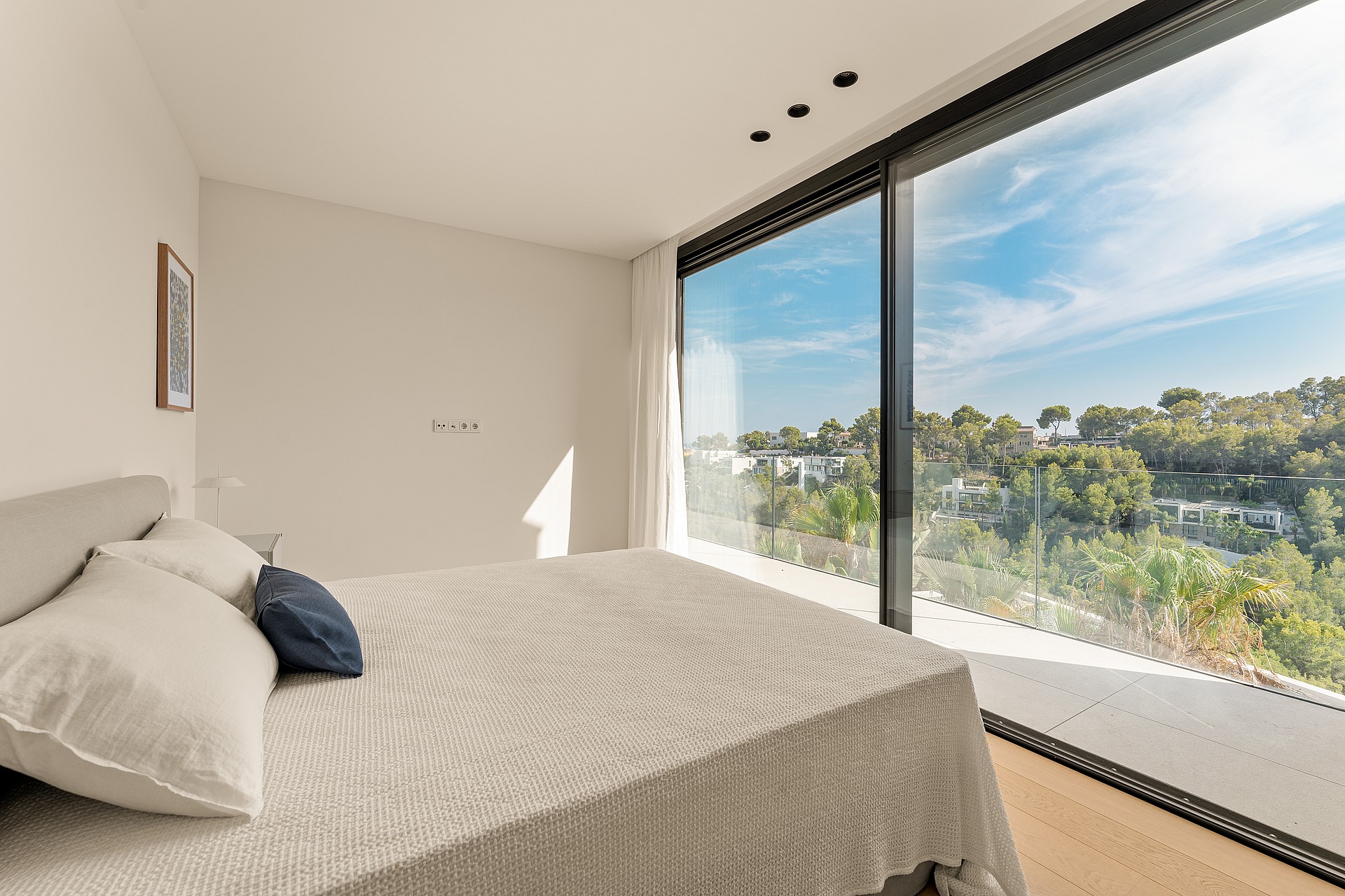 A modern bedroom with a large bed, featuring floor-to-ceiling sliding glass doors that open to a green landscape view.