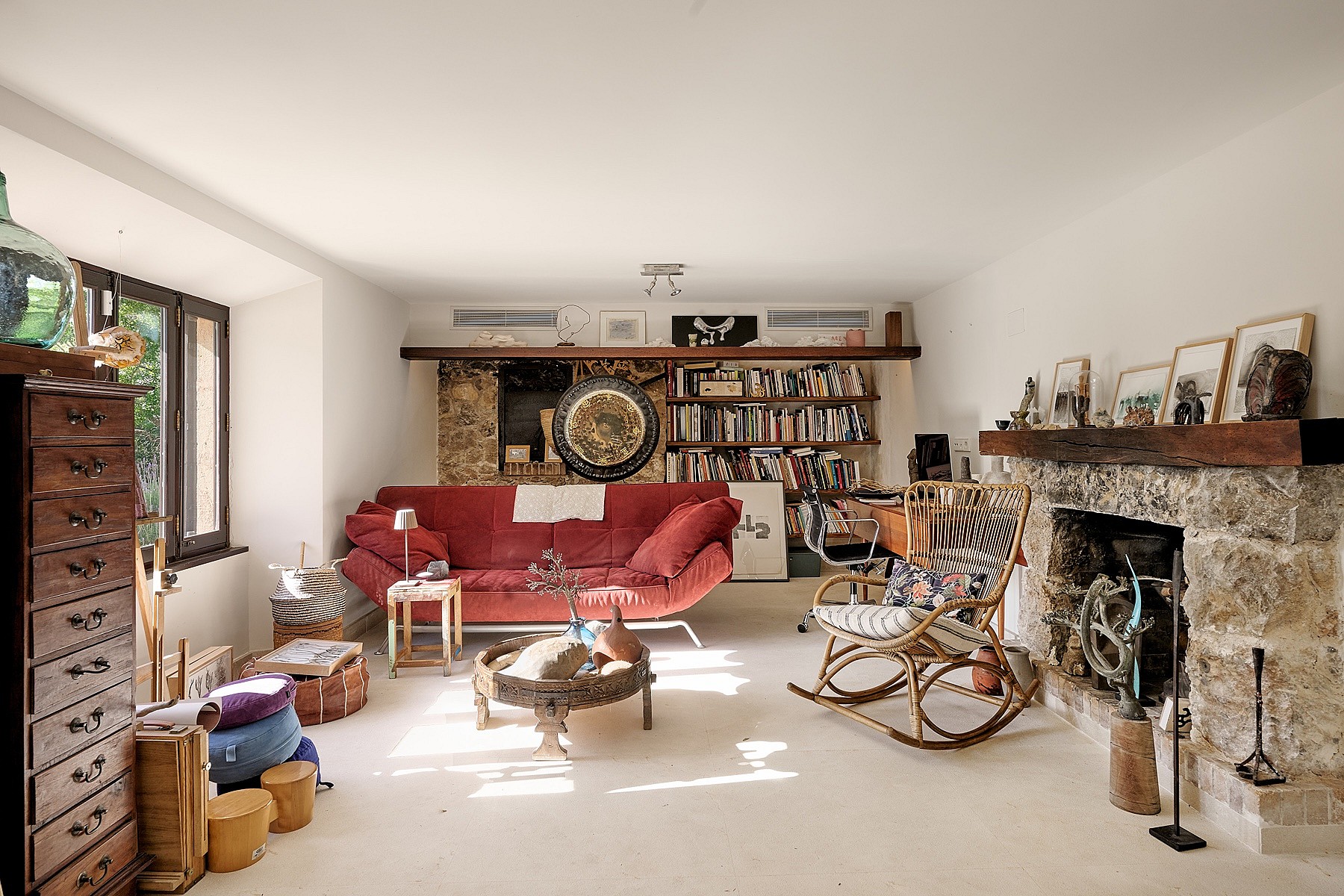 A living area in a Finca featuring a large stone fireplace, exposed wooden beams, a red sofa, and a wicker rocking chair.