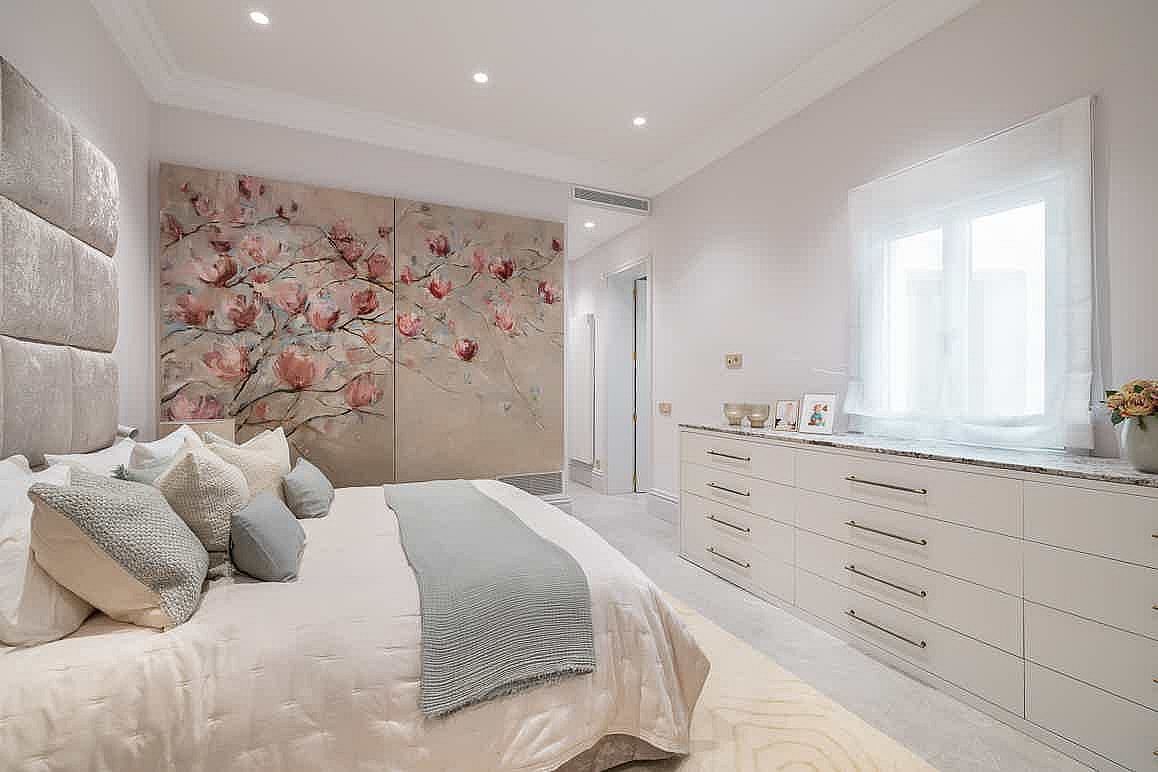 A modern bedroom featuring a large floral mural on the wall, a plush upholstered headboard, and an extensive white dresser.