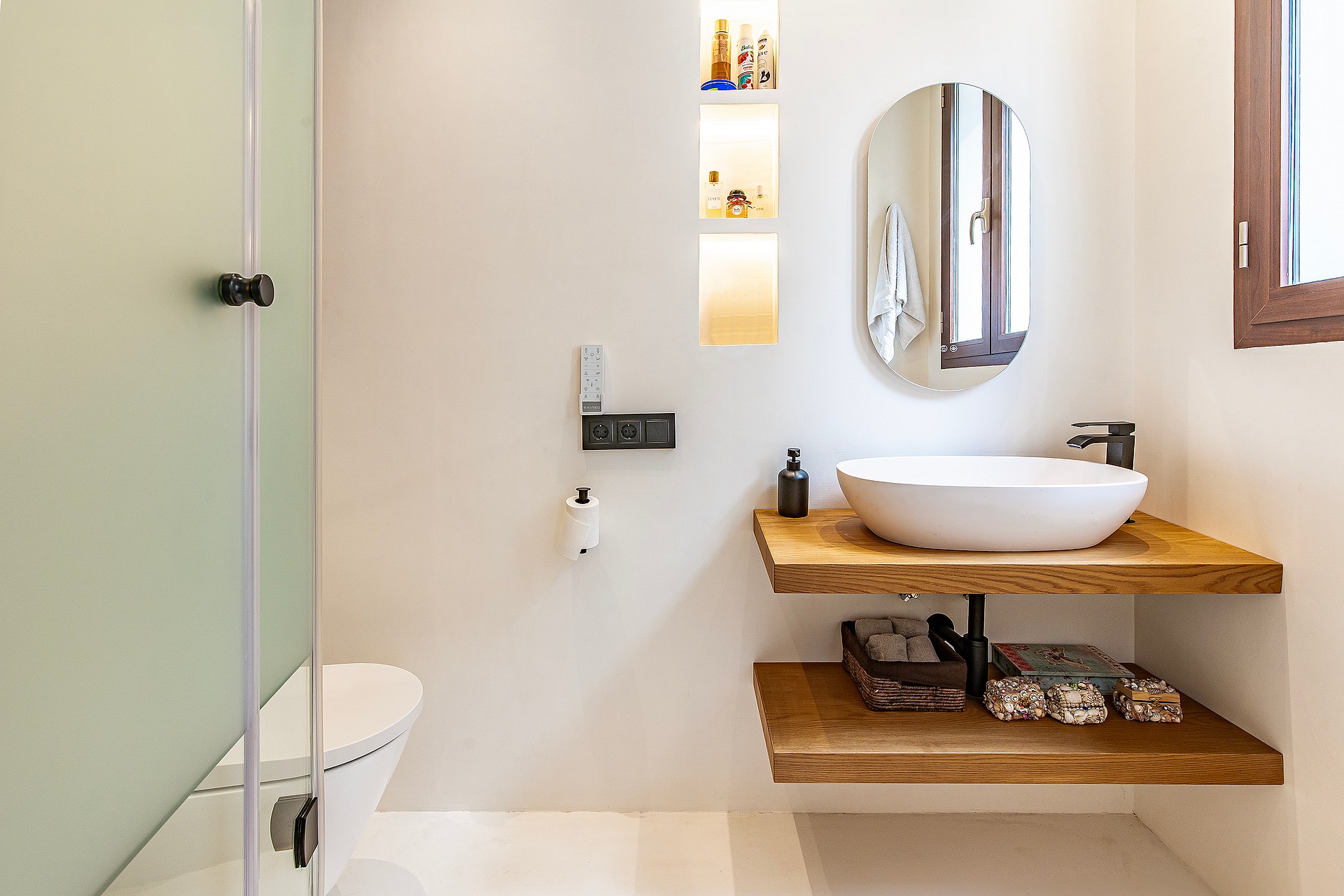 Modern bathroom featuring a floating double-tier oak vanity, white vessel sink, and an oval wall mirror against light walls.