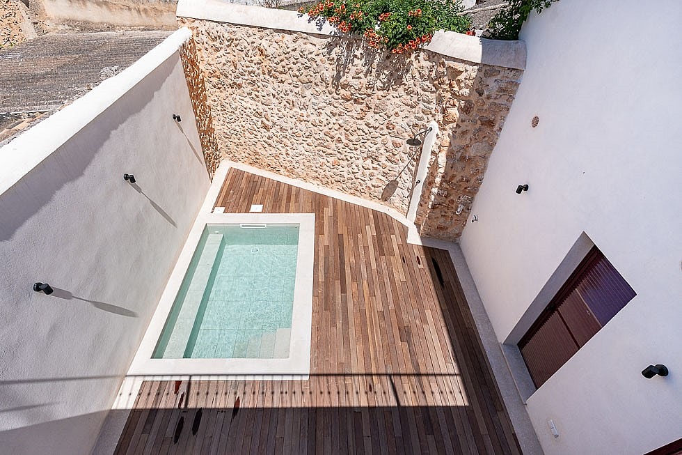 High-angle view of a small rectangular plunge pool surrounded by a wooden deck and high white walls with a natural stone feature wall.