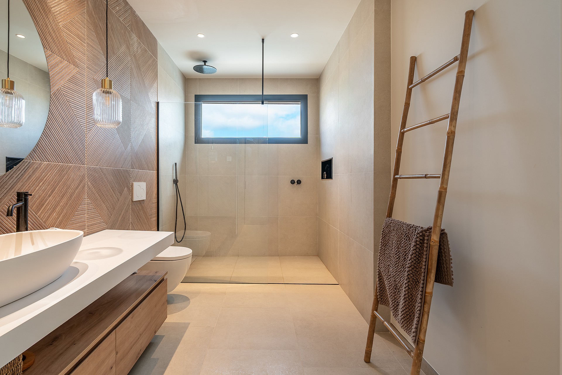 A contemporary bathroom featuring a white vessel sink on a floating wood vanity, a textured bronze accent wall, and a large walk-in shower area with a bamboo towel ladder.