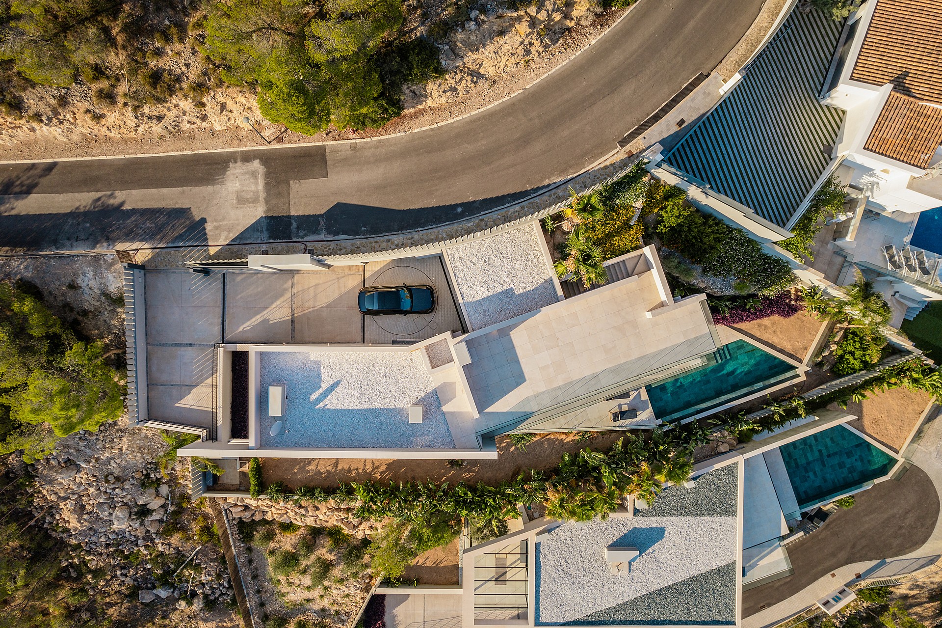 Top-down aerial view of a multi-level hillside villa showing rooftops, two swimming pools, stone terraces, and access road.