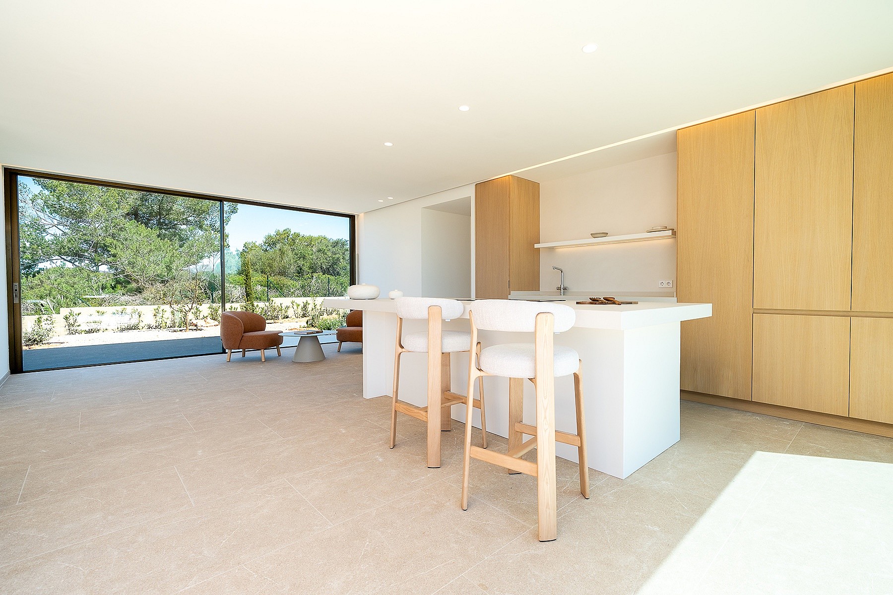 Modern open-plan kitchen with a white island, wooden cabinetry, and large sliding glass doors overlooking mountain scenery.