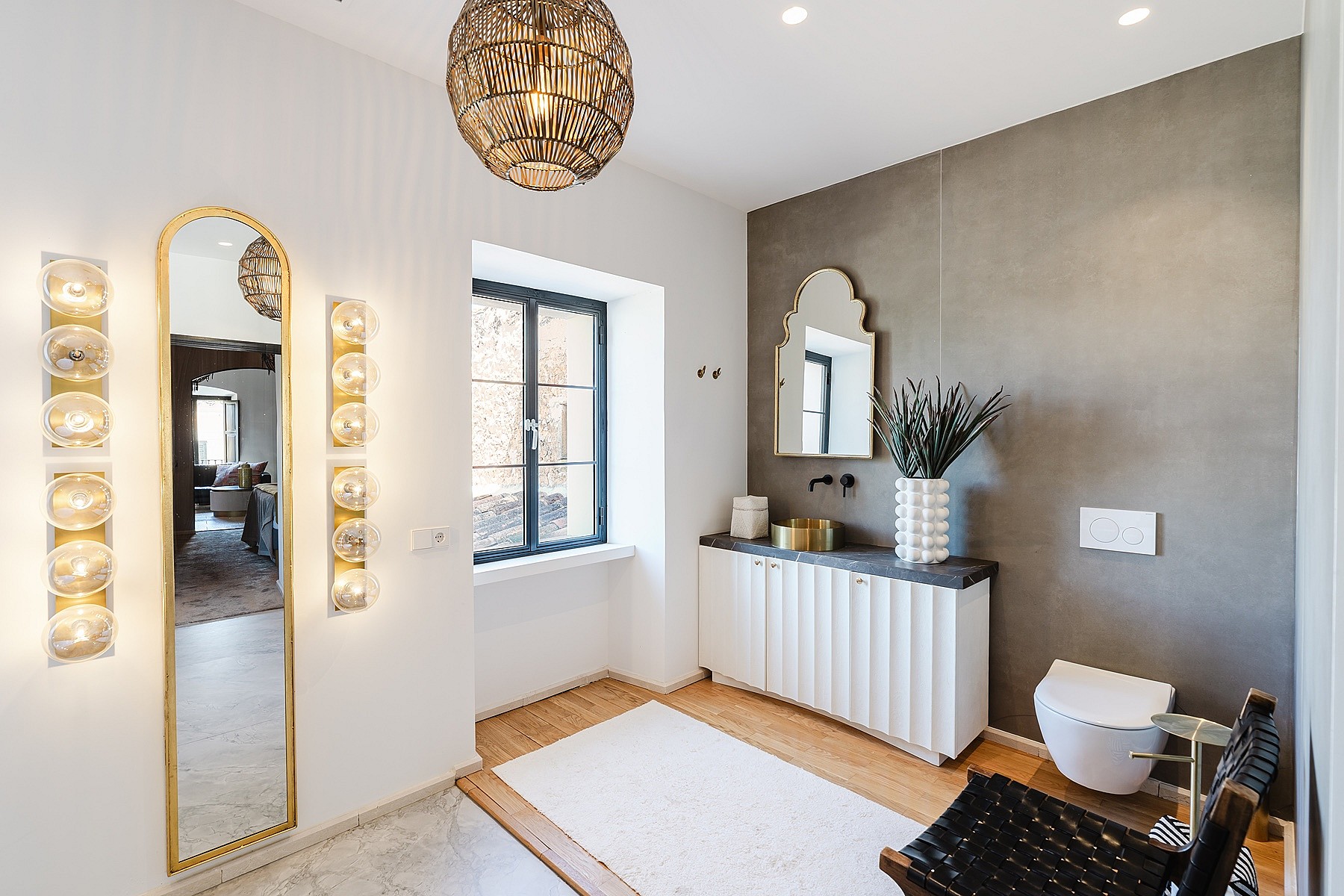 Bathroom with white fluted vanity, gray accent wall, arched mirror, and warm pendant lighting.