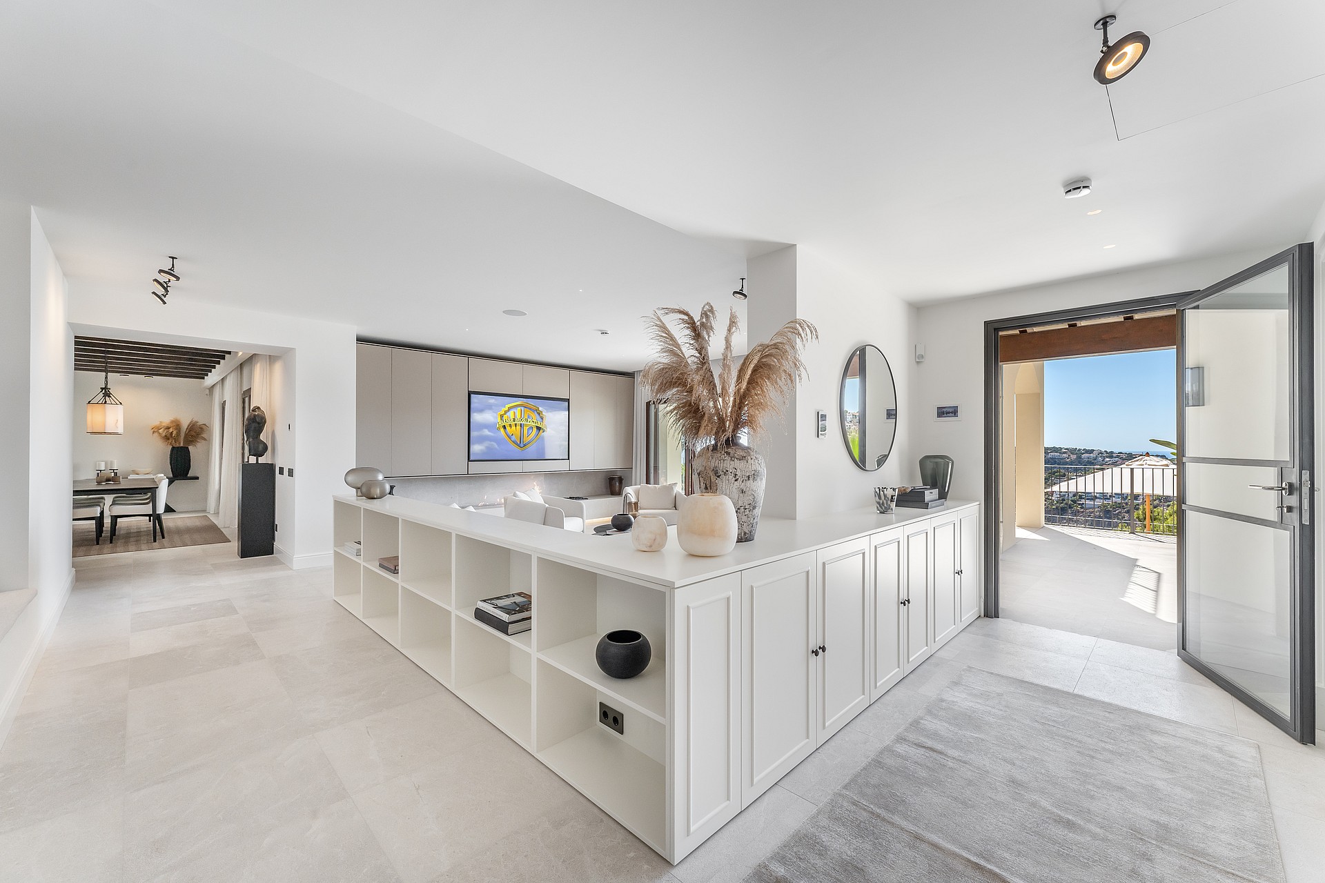 Sunlit hallway featuring white built-in storage and an open glass door leading to a terrace with distant views.