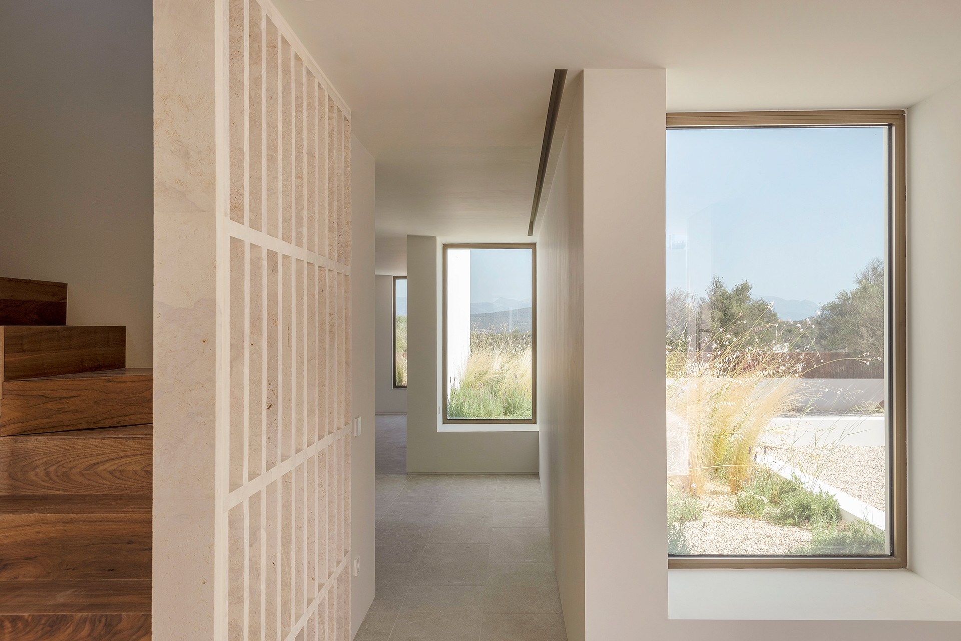 Minimalist hallway with a decorative stone partition and large windows viewing a Mediterranean garden.