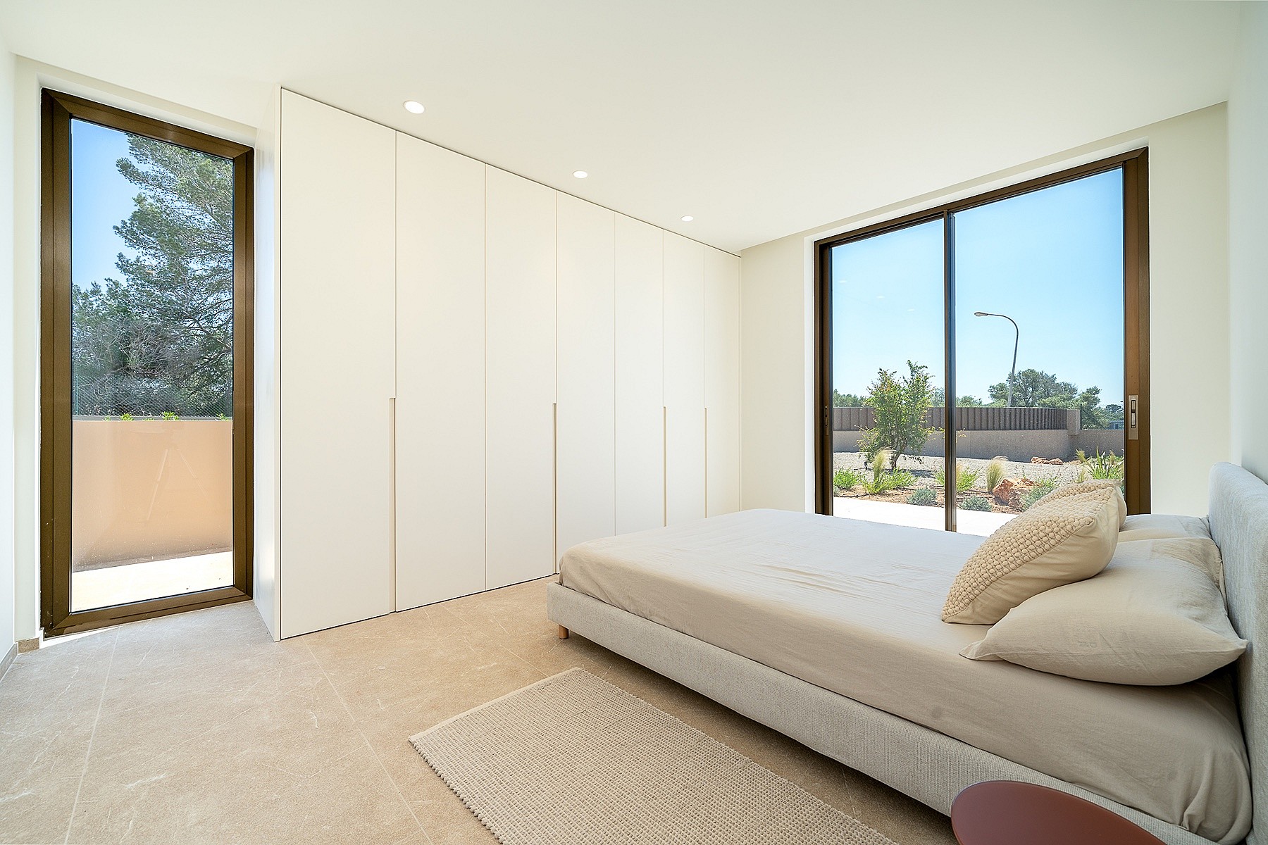 Modern bedroom with a large white floor-to-ceiling built-in wardrobe, a neutral bed, and sliding glass doors opening to a terrace.