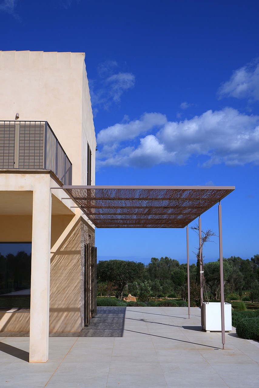 Exterior terrace of a Mallorcan finca with a metal laser-cut pergola casting intricate shadows on the stone floor.
