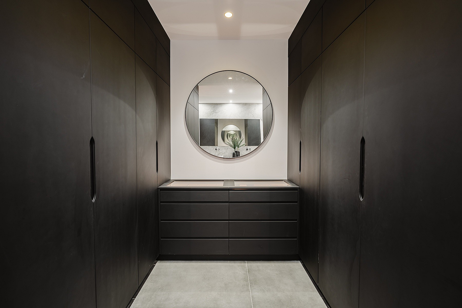 Symmetrical walk-in closet featuring floor-to-ceiling matte black cabinets, a central vanity drawer unit, and a round mirror.