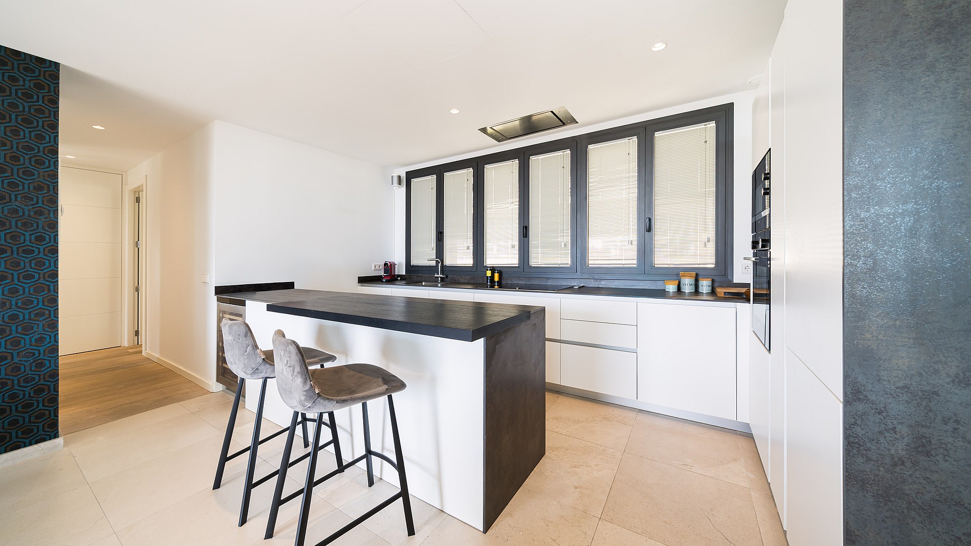 A minimalist kitchen featuring white handleless cabinetry, a dark grey island, and large dark-framed windows.
