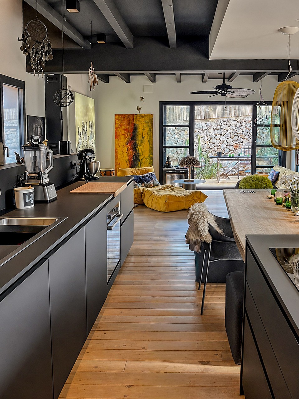 Contemporary kitchen with matte black cabinetry and wooden floors leading to an outdoor terrace with stone wall views.