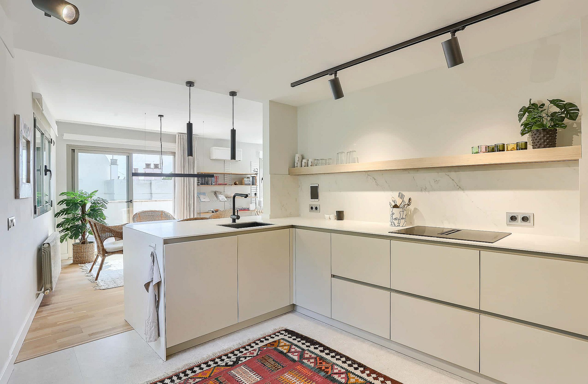 A contemporary white kitchen featuring a peninsula island, track lighting, and a patterned rug on the floor.