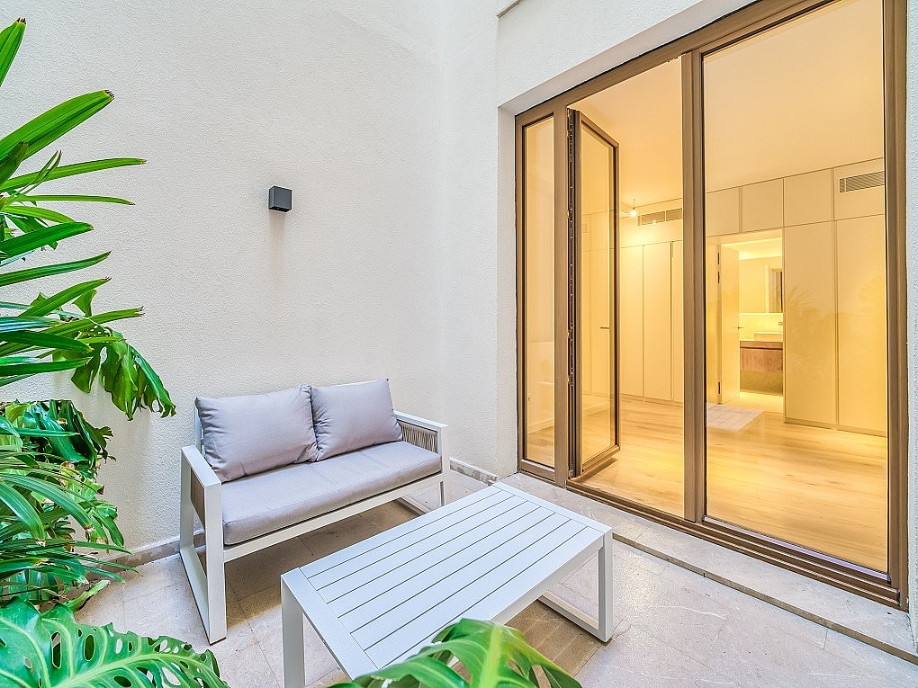 A small outdoor terrace with a two-seater sofa and coffee table next to large glass doors leading into an interior room.