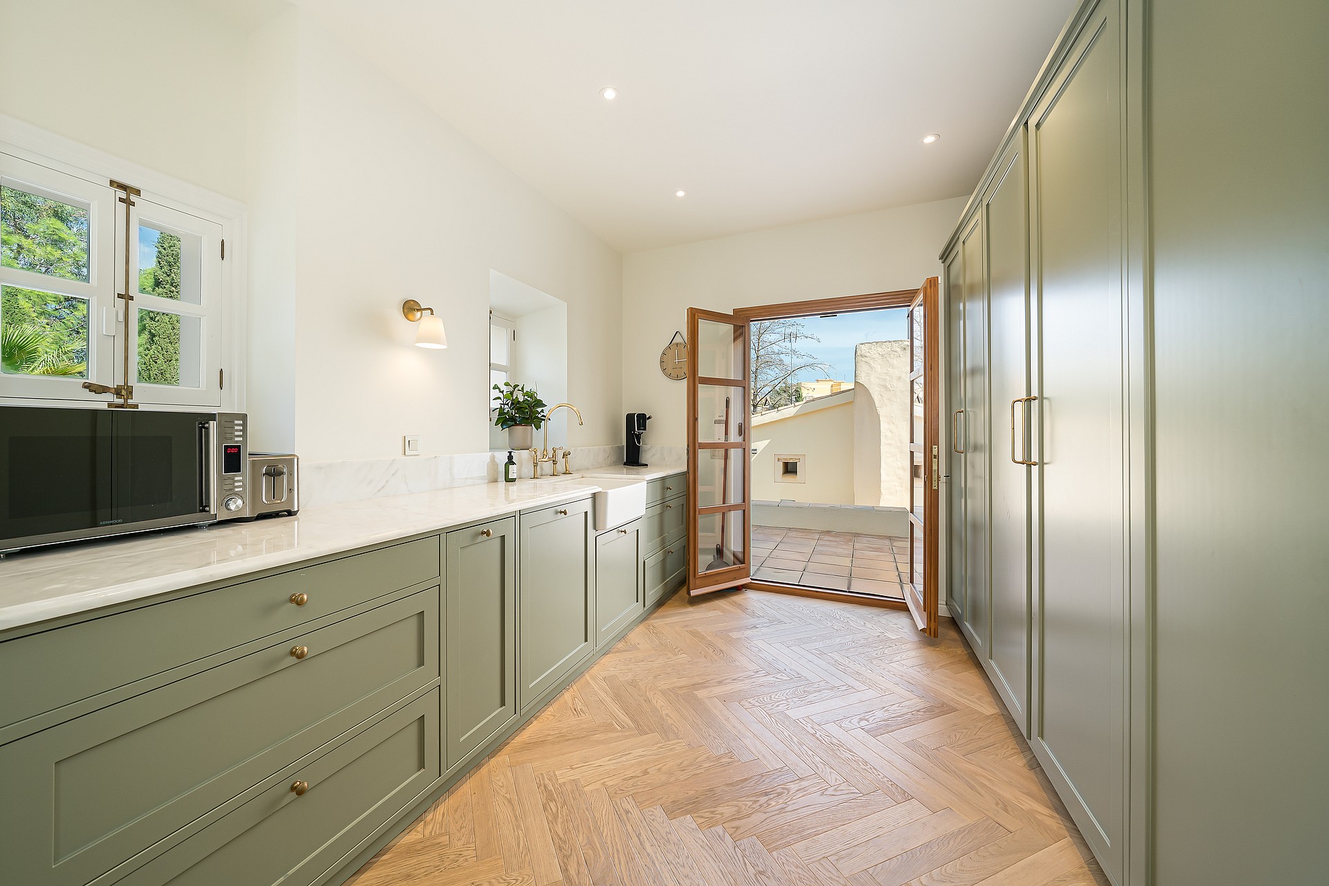 Contemporary kitchen featuring sage green shaker cabinets, white stone countertops, and light oak herringbone floors.