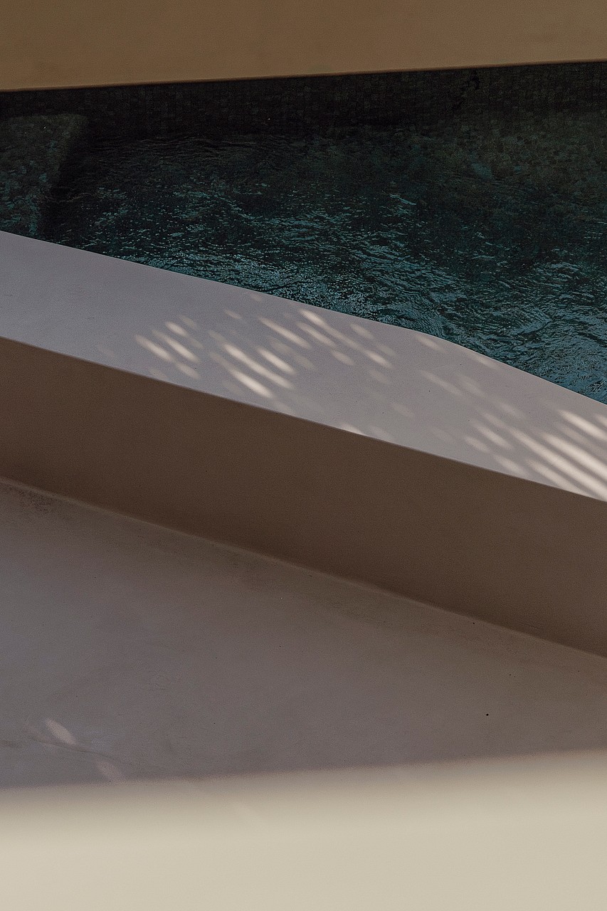 A close-up of a swimming pool edge featuring dark water and a smooth, neutral-toned concrete or stone coping.