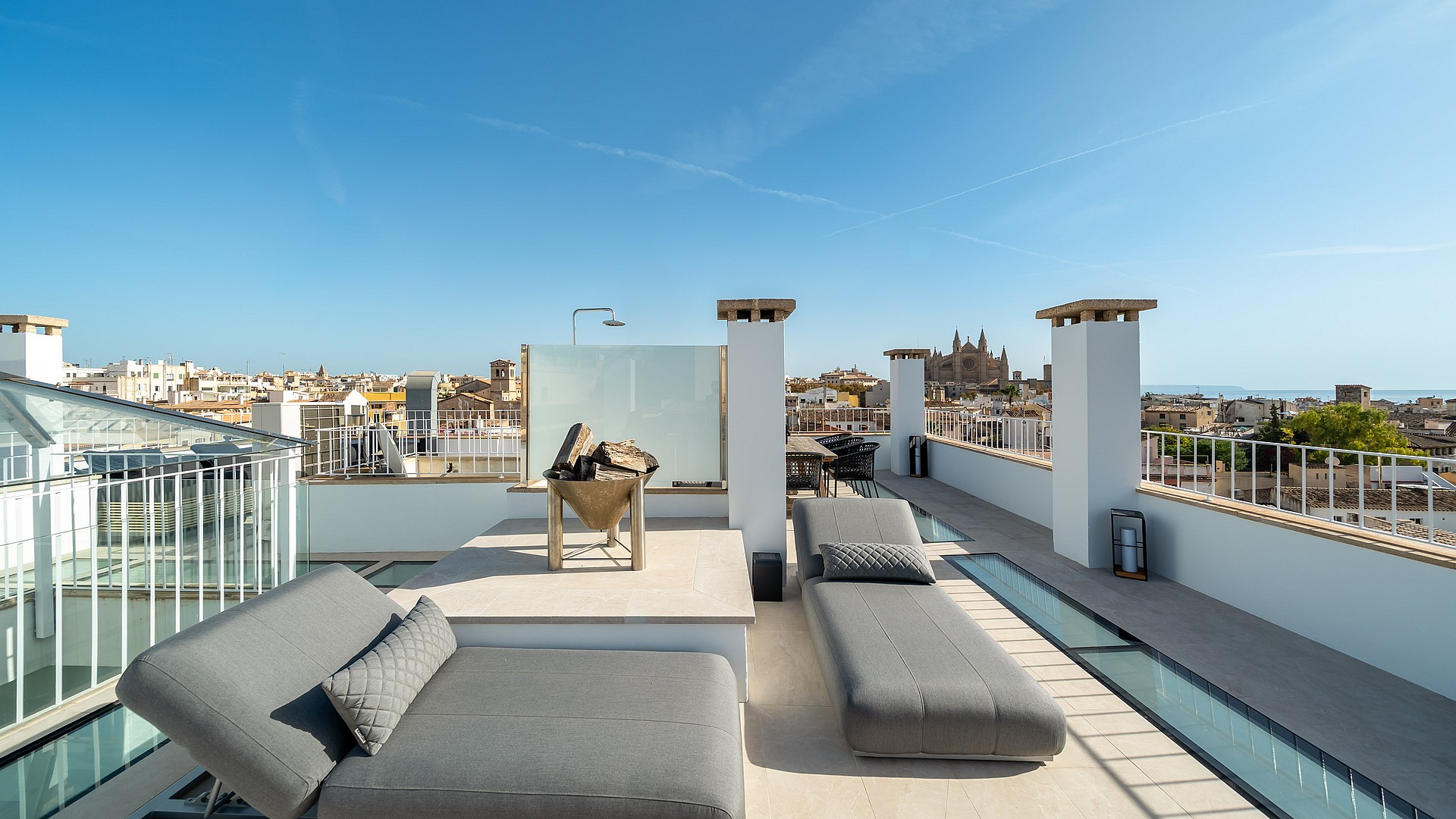 Sun-drenched rooftop terrace with grey loungers, stone flooring, and panoramic views of Palma's historic skyline.