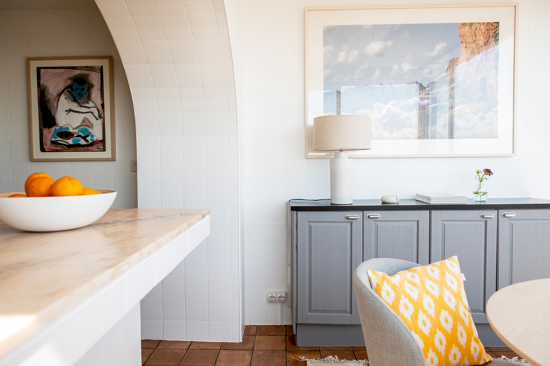 Interior view showing a white brick arch leading to a room, a grey sideboard with a table lamp, and a yellow patterned cushion.
