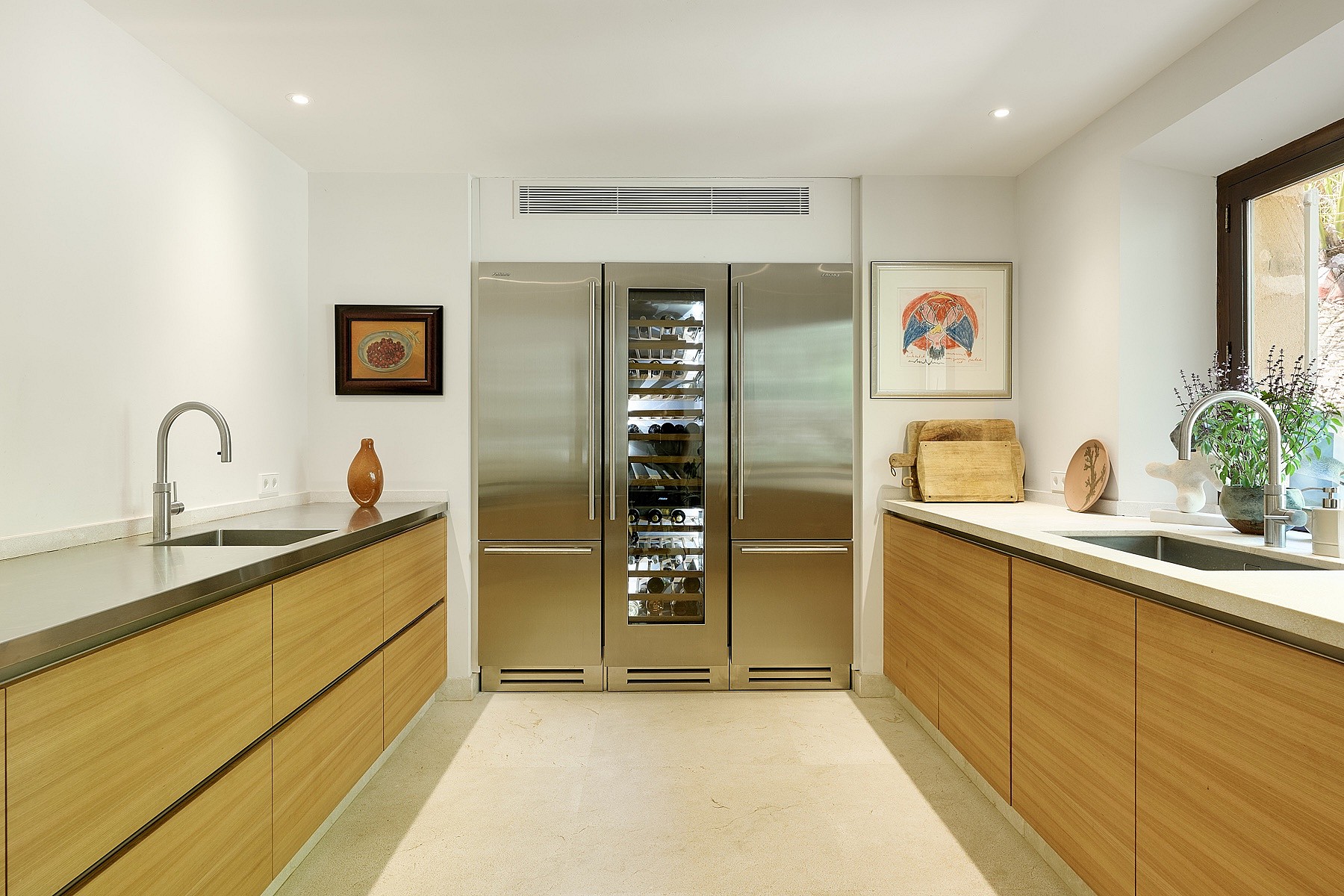 A modern galley kitchen featuring oak cabinetry, stainless steel appliances, and a central glass-fronted wine fridge.