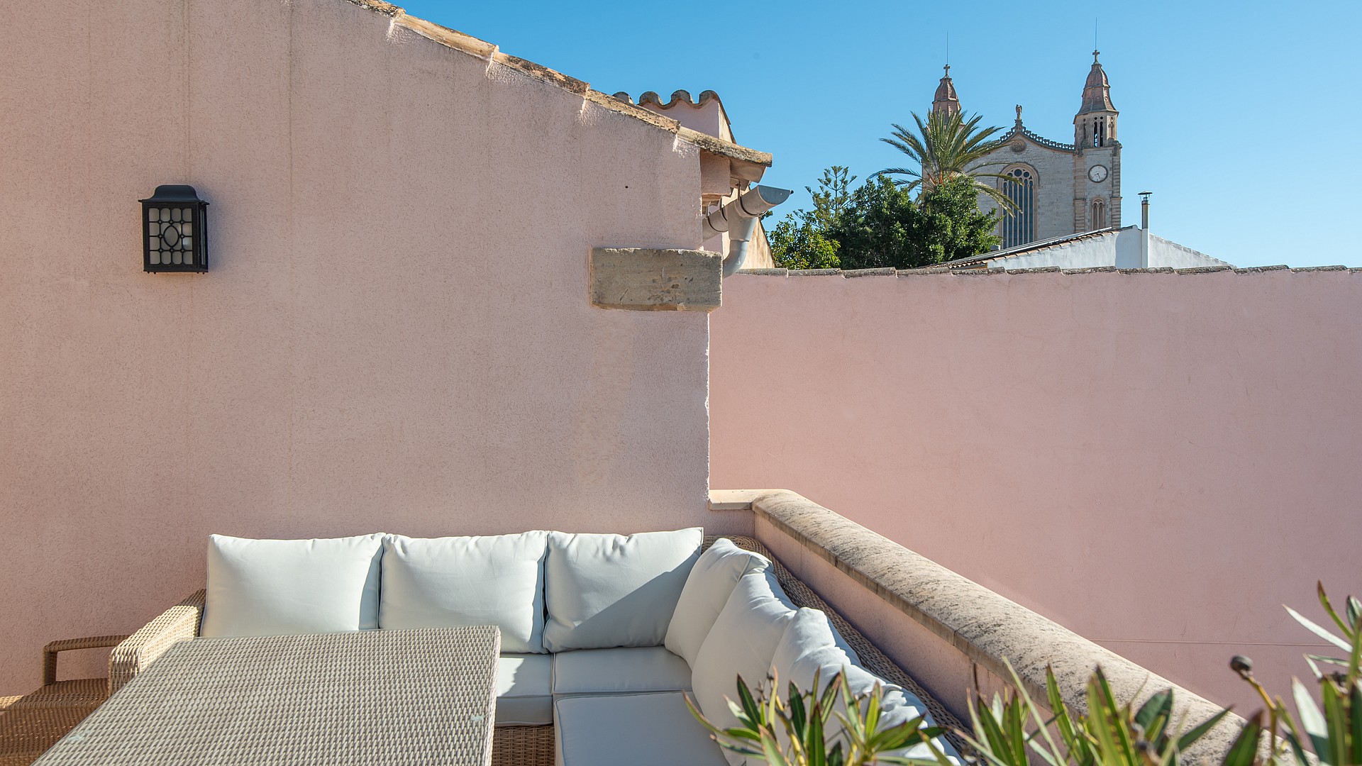 Outdoor terrace featuring exterior sofas, soft pink walls, and views towards the church tower in Calvià.