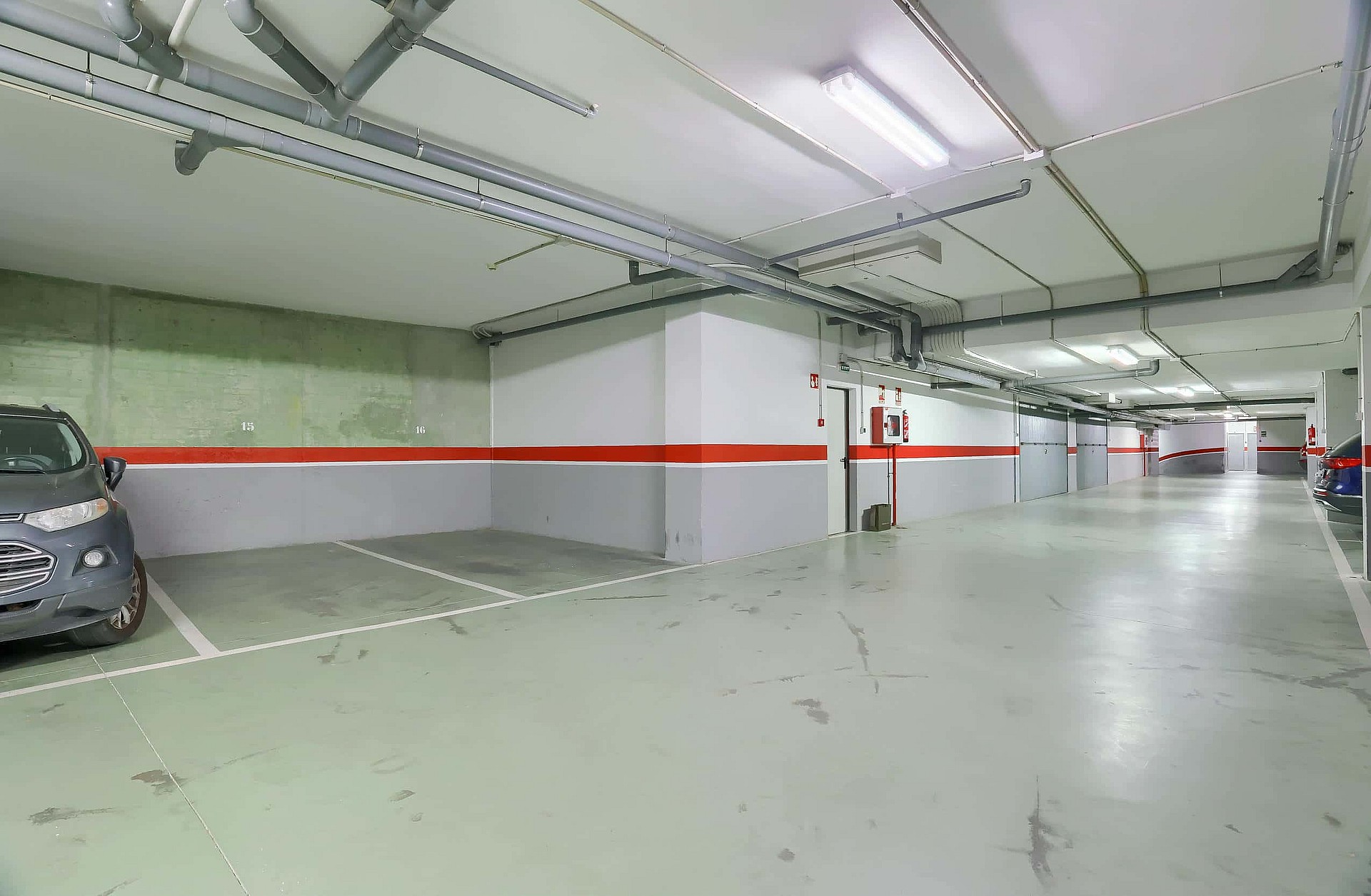 A clean, well-lit underground parking garage with white and grey walls, red accent stripes, and marked parking spaces.