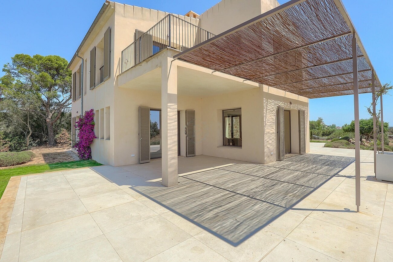 Exterior view of a beige stone finca in Santanyí featuring a large patio covered by a natural reed pergola.