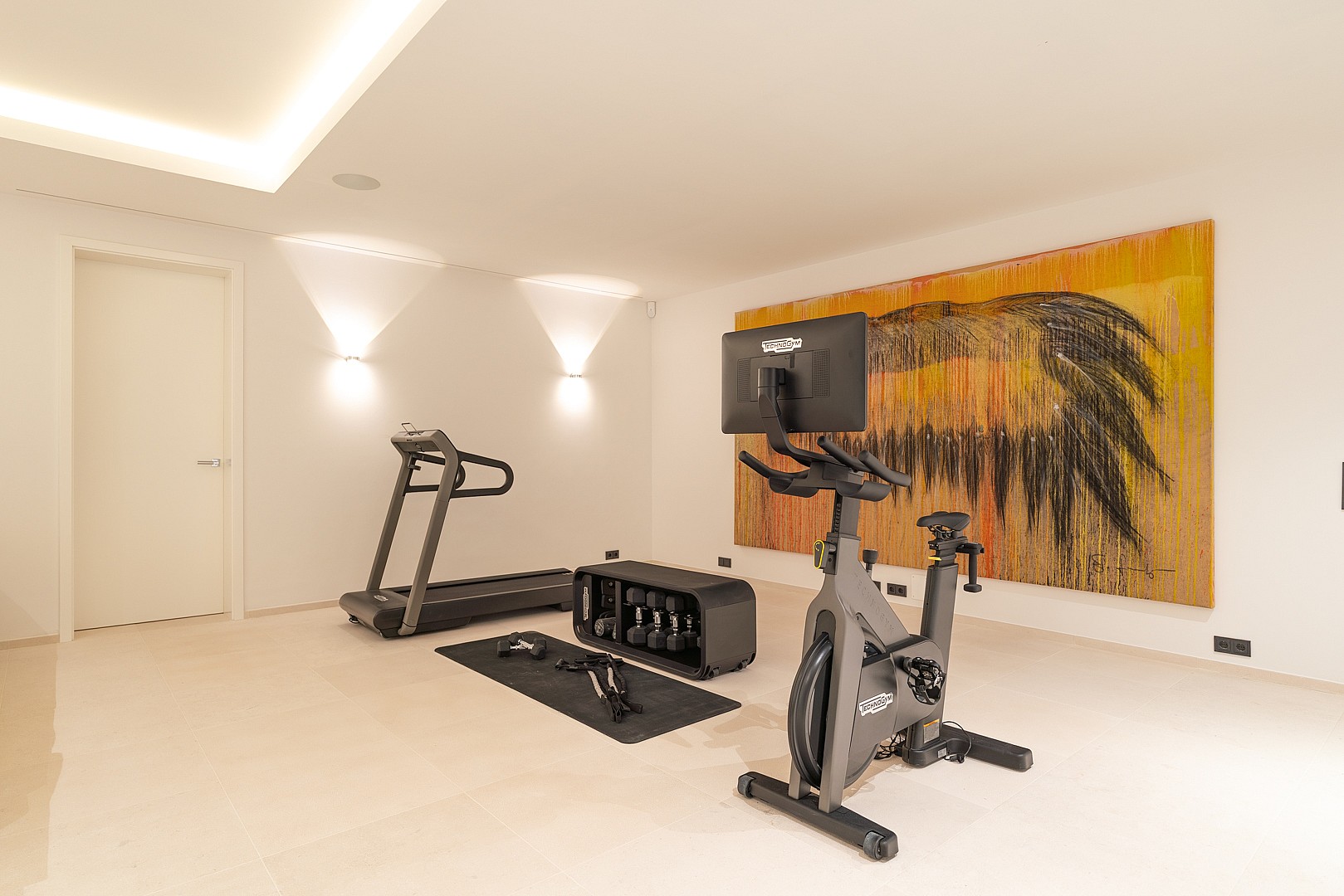A minimalist home gym featuring a stationary bike, a treadmill, and a rack of dumbbells set against a large abstract painting.