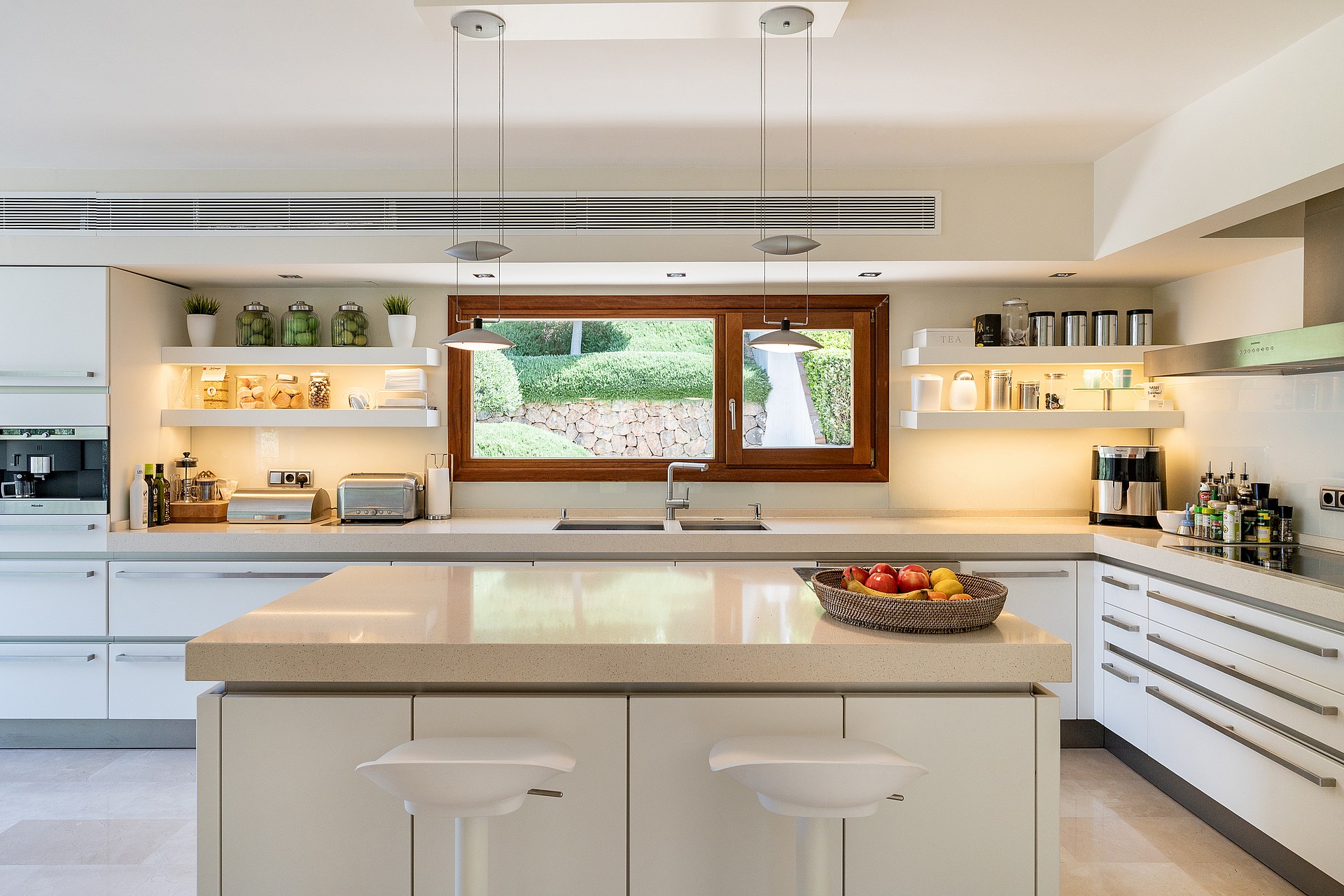 Fully fitted kitchen with white cabinetry, stone worktops, central island, Miele ovens and garden window