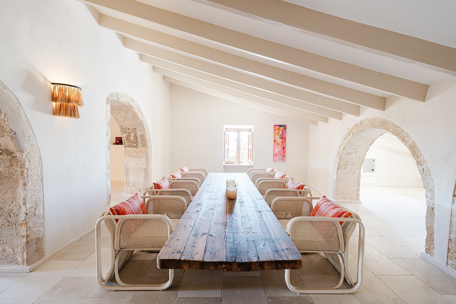 Dining room with a long wooden table, rattan chairs, and exposed stone arches under a pitched timber beam ceiling.